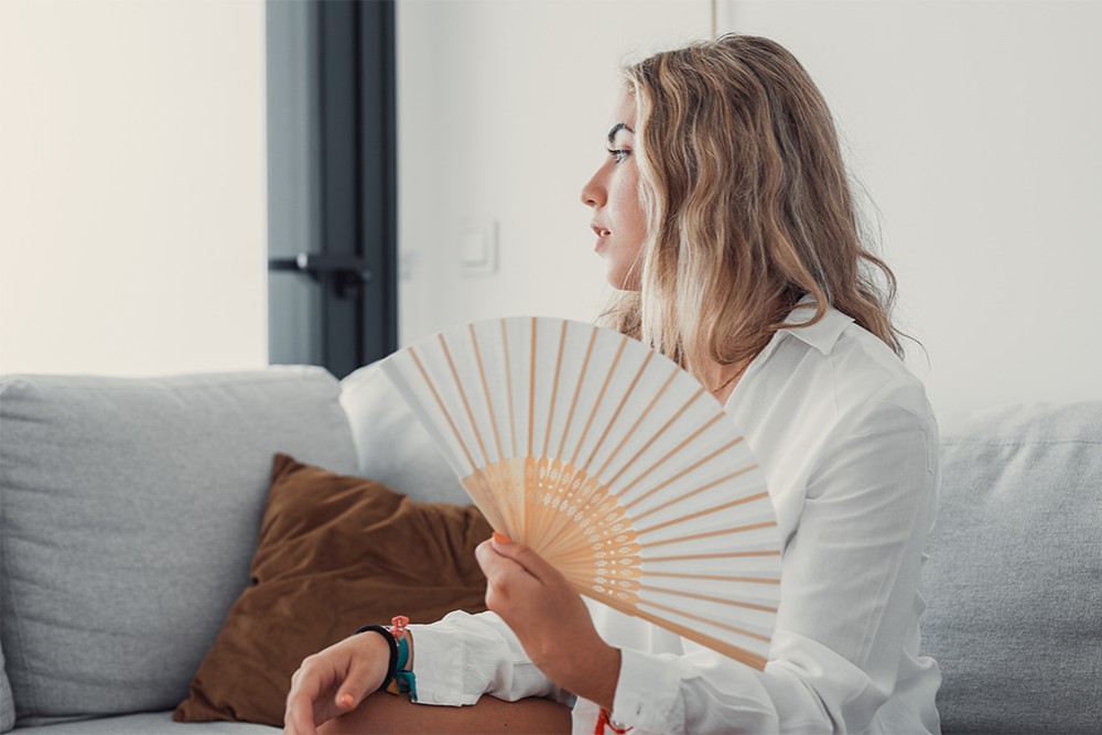 Woman using a hand fan as a conscious way to keep cool this summer