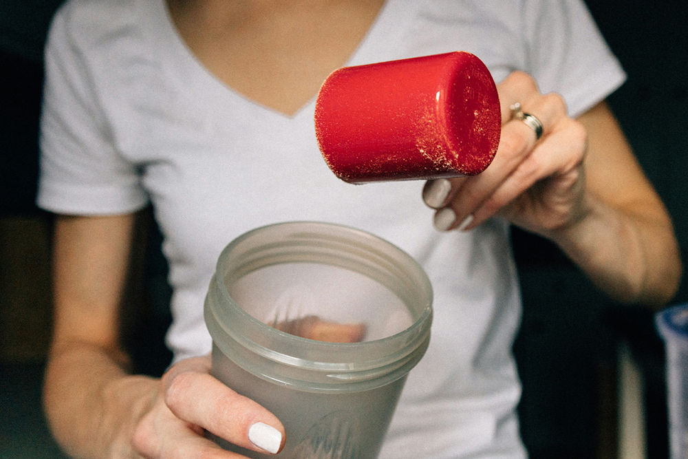 Woman pouring natural protein powder into a Nutribullet