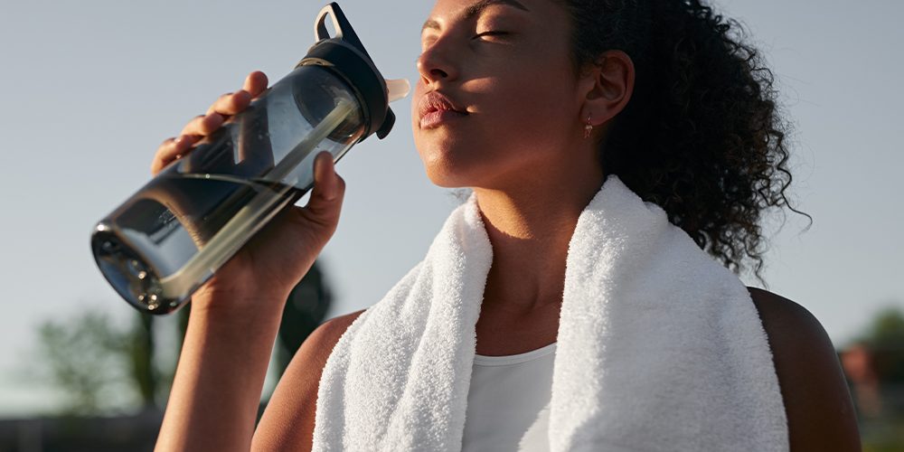 Women drinking water from a water bottle with a towel around her neck