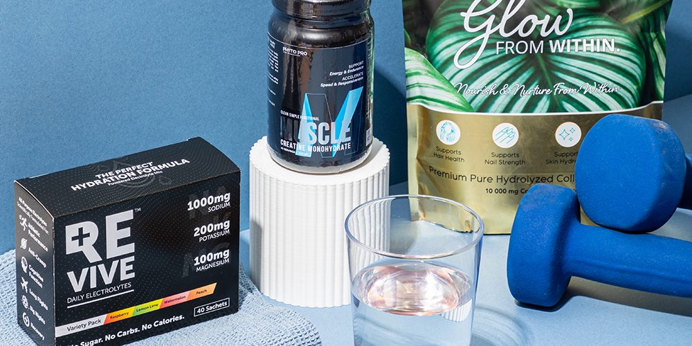 Sports nutrition supplements including electrolytes, creatine and collagen displayed with dumbbells and a glass of water on a blue background.