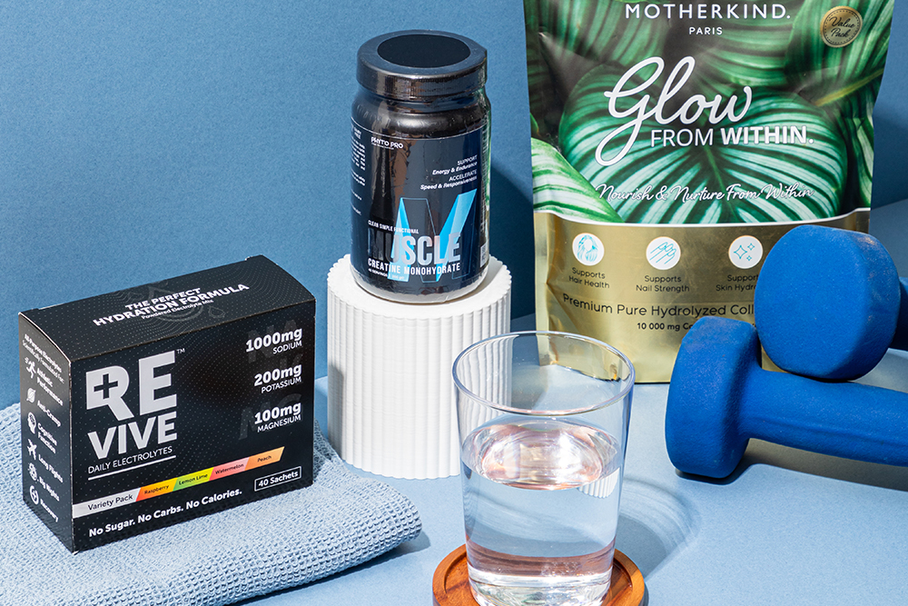Sports nutrition supplements including electrolytes, creatine and collagen displayed with dumbbells and a glass of water on a blue background.
